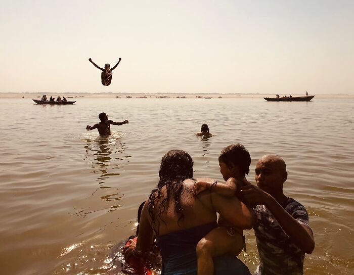 Children swimming and playing in a river with boats in the distance, capturing the essence of exploring Asia through photography.