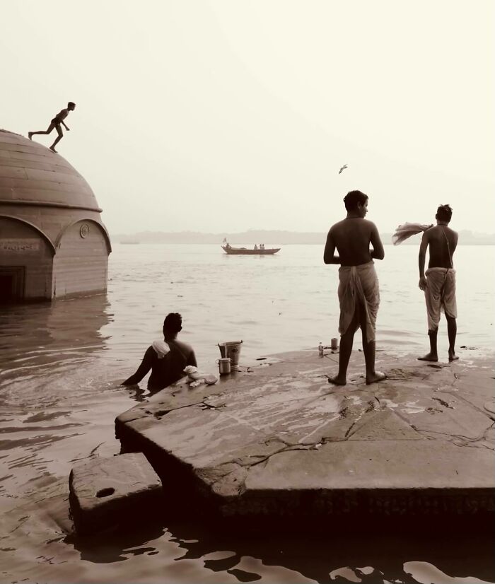Three men at a riverbank preparing to bathe, a boy climbing a dome, and a boat floating on the water in Asia.