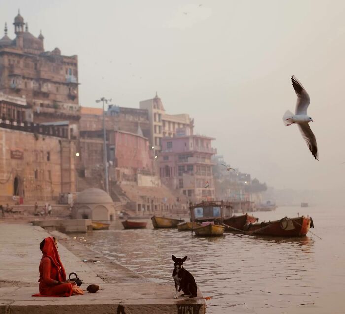 Woman in red sitting by the river with boats and historic buildings, capturing the essence of exploring Asia photography.