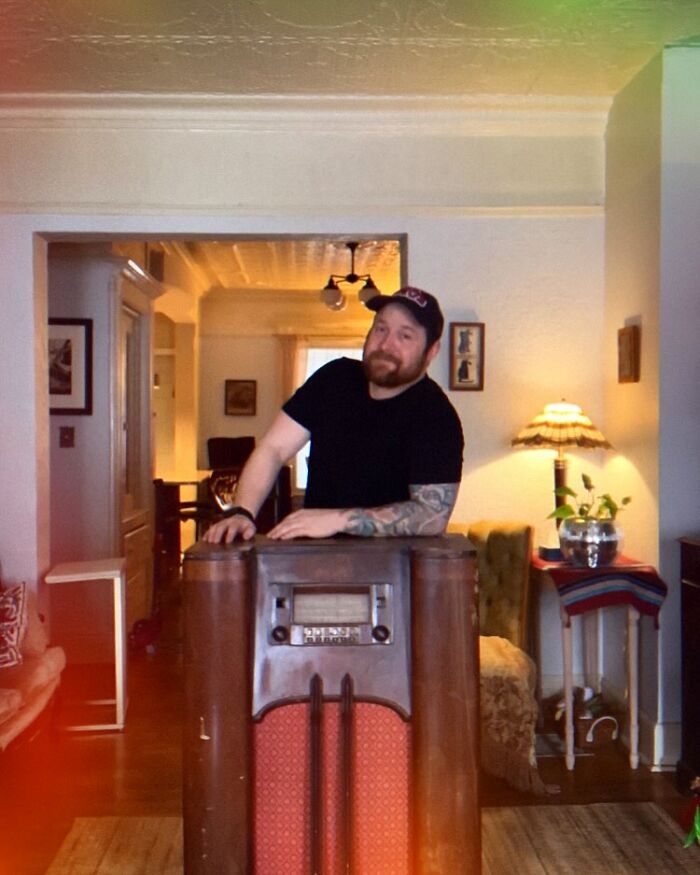 Man leaning on a vintage TV turned into a cozy cat bed in a warmly lit nostalgic nook at home