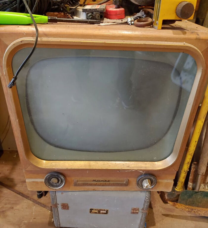 Vintage TV turned into a cozy cat bed in a workshop filled with tools and nostalgic decor elements.