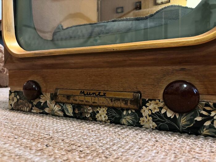 Close-up of a vintage TV base repurposed as a cozy cat bed with floral accents and wooden details.