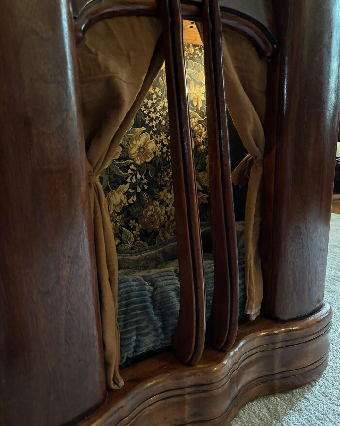 Vintage TV repurposed into a cozy cat bed with floral wallpaper and soft curtains inside a wooden frame.