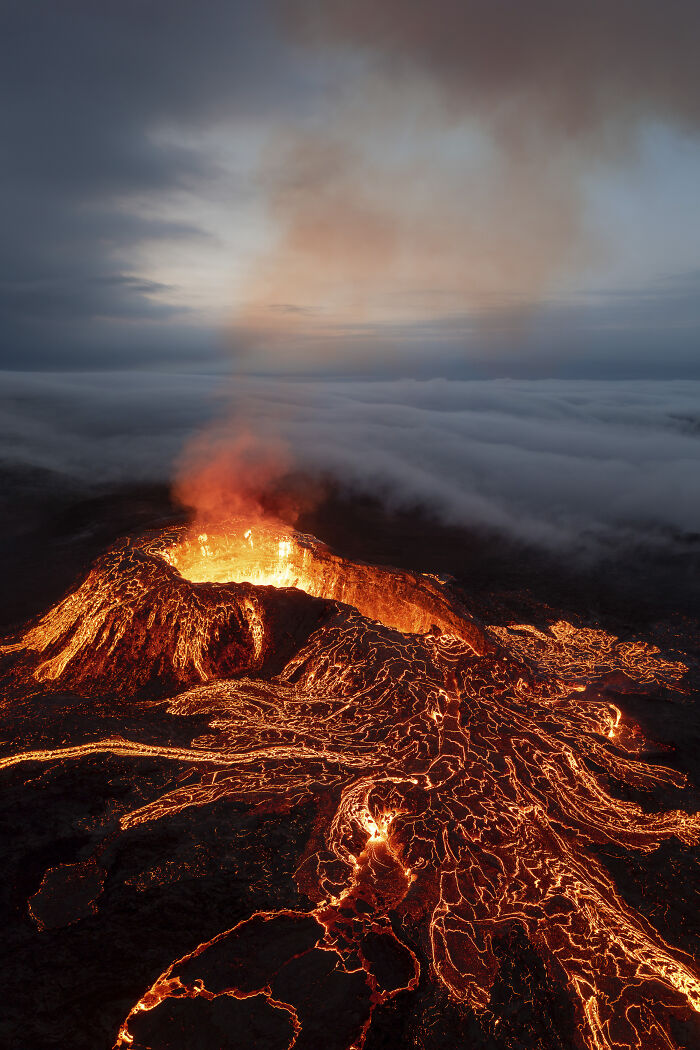Aerial shot of an erupting volcano with flowing lava and glowing smoke captured in dramatic light.