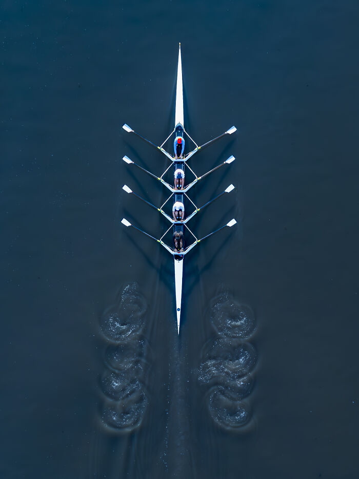 Aerial shot of a rowing team on dark blue water creating circular wake patterns in a synchronized motion.