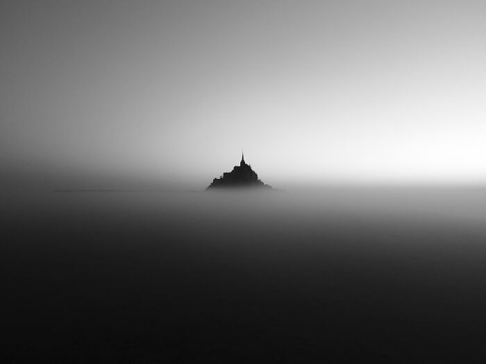 Aerial shot of a solitary mountain peak rising above dense fog in a minimalist black and white landscape.