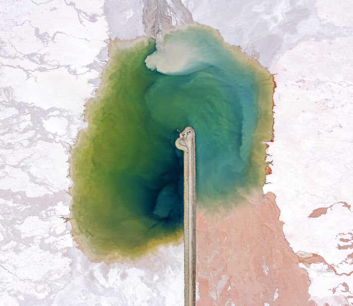 Aerial shot of a colorful lake with a narrow pier extending into the water, showcasing winning aerial photography.