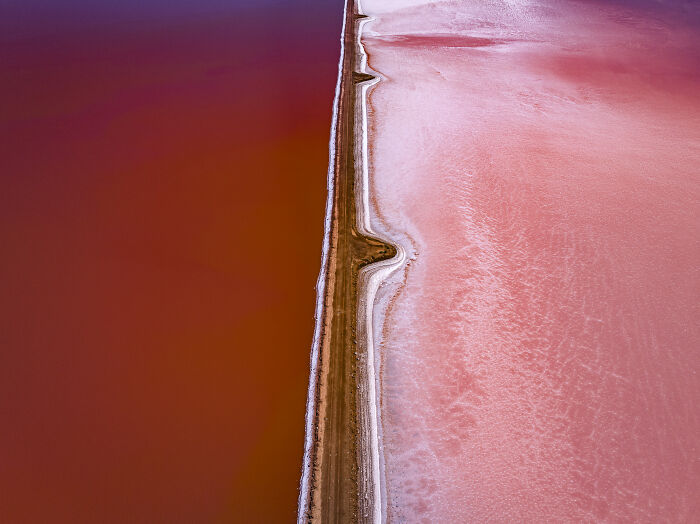 Aerial shot of contrasting red and pink salt lakes separated by a narrow land strip, showcasing winning aerial photography.