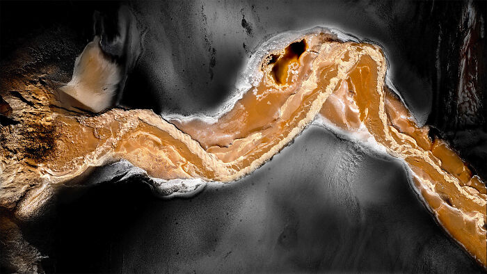 Abstract aerial shot showing winding orange river contrasting with dark surrounding terrain in winning aerial shots collection.