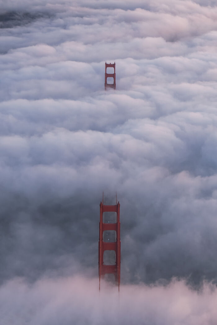 Aerial shot of the Golden Gate Bridge towers rising through dense fog, showcasing winning aerial photography.