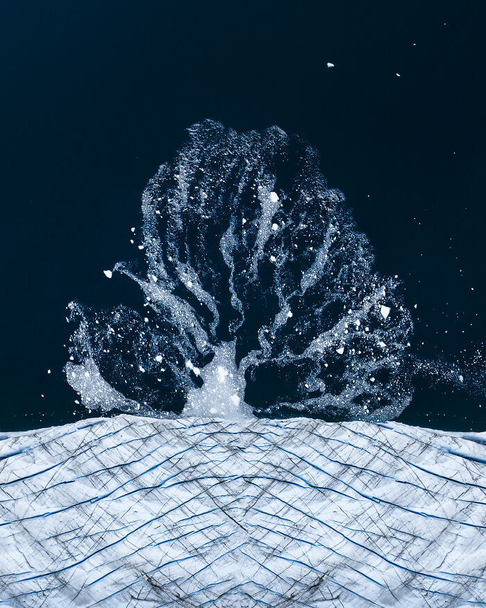 Aerial shot of ice splashing to form a dramatic pattern over frozen landscape, captured in winning photography style.