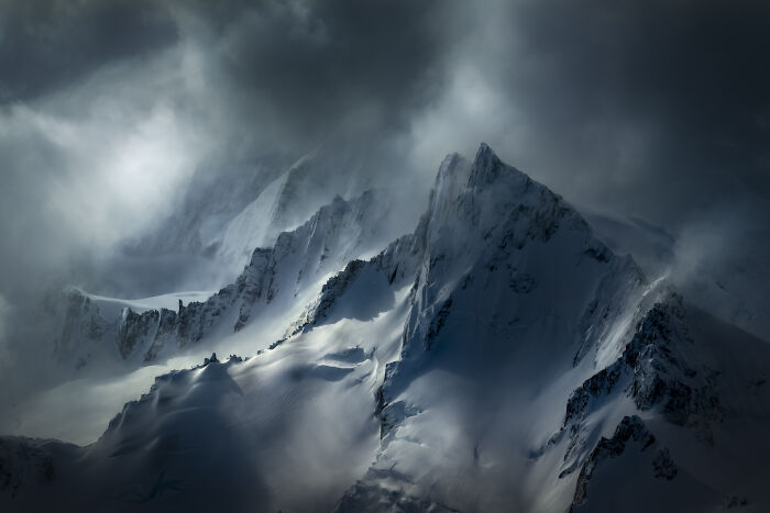 Dramatic aerial shot of snow-covered mountain peaks under dark, moody clouds from winning aerial shots photographer.
