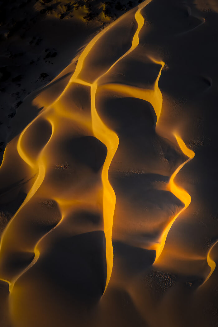 Aerial view of sand dunes illuminated by golden light showcasing abstract patterns in a winning aerial shot.