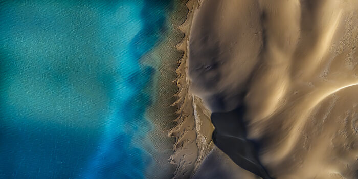 Aerial shot of sandy desert dunes meeting vibrant turquoise water showcasing winning aerial shots photography.