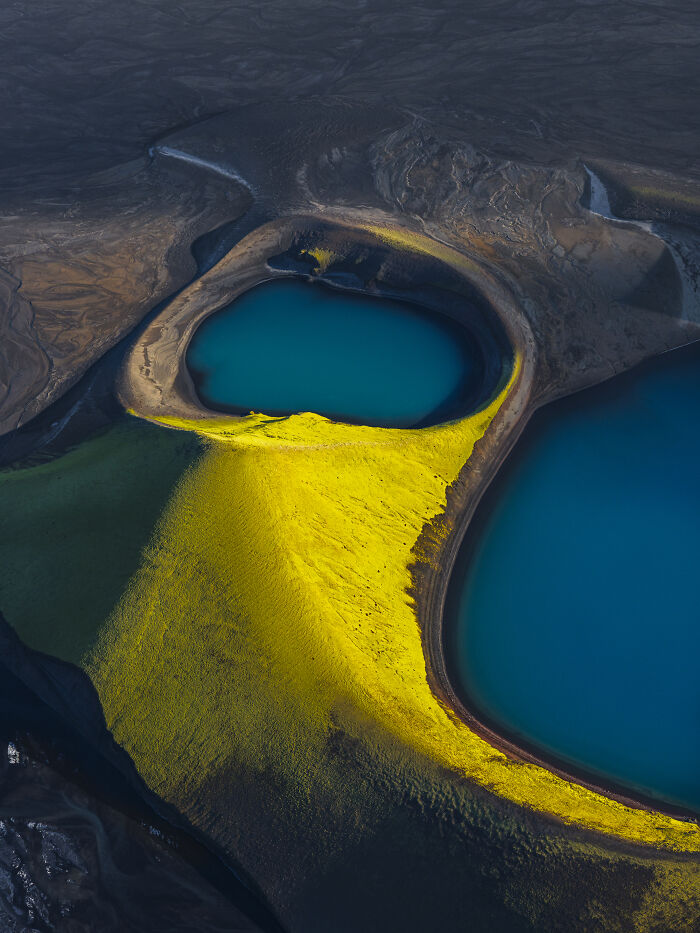 Aerial shot of a vibrant landscape with dark waters and mossy yellow-green terrain in natural light.