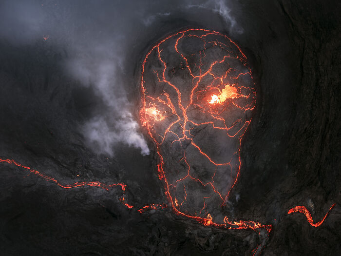 Aerial shot of glowing lava patterns forming a skull shape, captured in a winning photograph of the International Photographer of the Year.