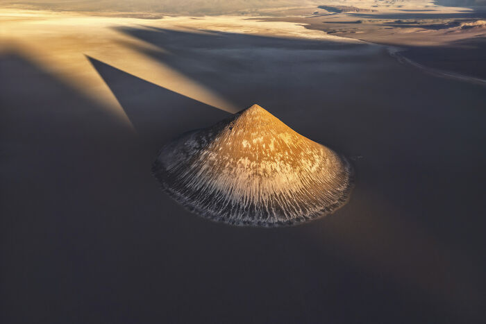 Aerial shot of a sunlit volcanic mountain casting a long shadow over a vast desert landscape at sunset.