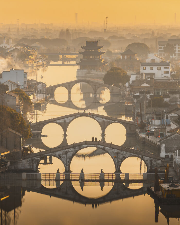 Ancient arched bridges and traditional buildings reflected in calm water at golden hour aerial shot