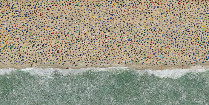 Aerial shot of a crowded beach with colorful umbrellas and waves, showcasing winning aerial photography.