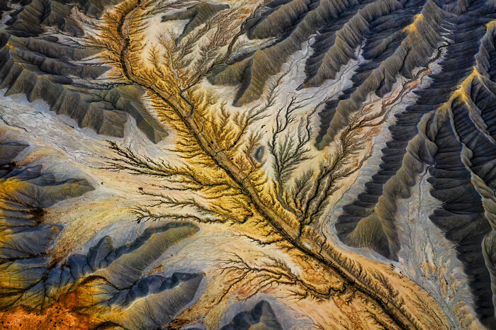 Aerial shot of rugged terrain with winding gullies and ridges showcasing natural geological patterns and textures.