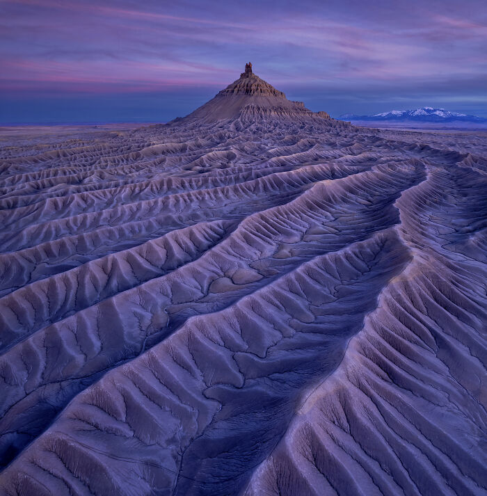Aerial shot of rugged terrain with ridges and a prominent peak under a purple and blue sunset sky.