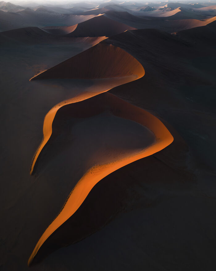 Aerial shot of illuminated sand dunes casting shadows in a vast desert landscape during golden hour light.