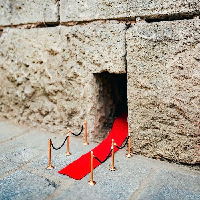 Tiny street scene of a red carpet leading into a small hole in the wall, part of funny miniature street art display.