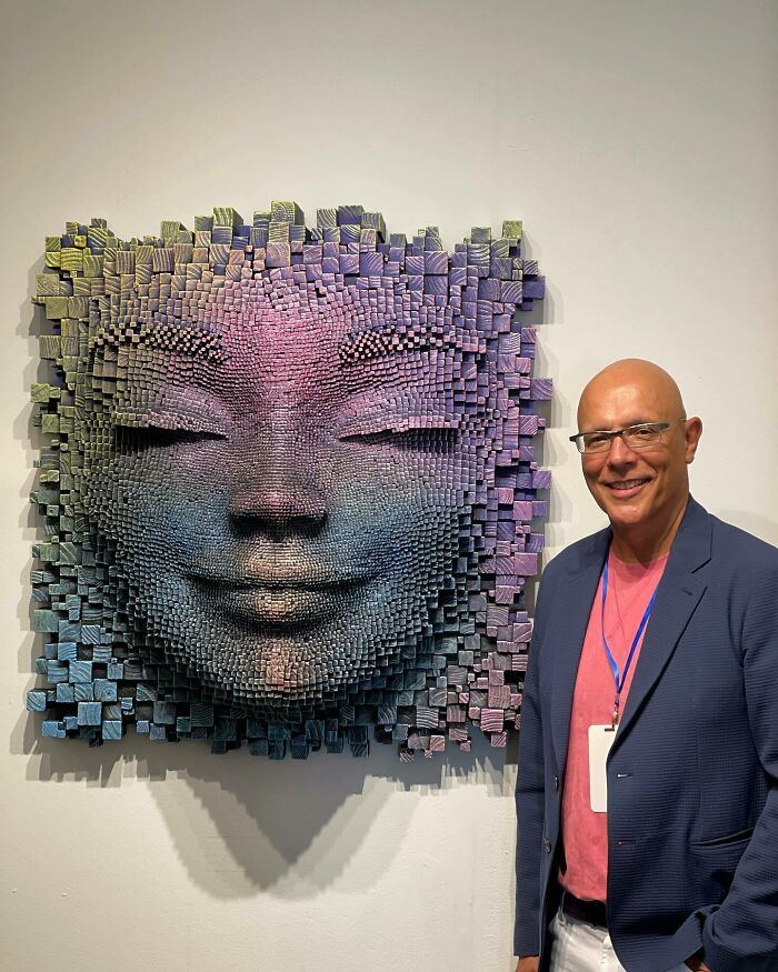 Man standing next to a hypnotic 3D wooden face sculpture made of colorful wooden sticks that seem alive.