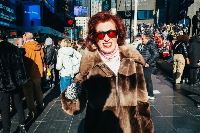 Woman in a fur coat and sunglasses smiling in a crowded NYC street, capturing vibrant street photos of city life.