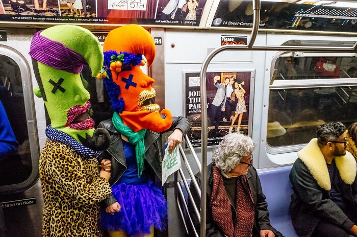 Two people in vibrant colorful masks and costumes riding a New York City subway, showcasing striking street photos.