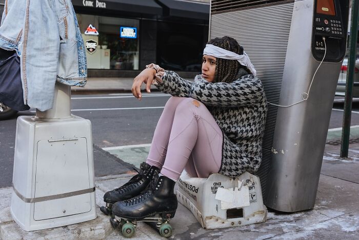 Young woman in roller skates sitting on a box on a NYC sidewalk in a striking street photo capturing city life moments.