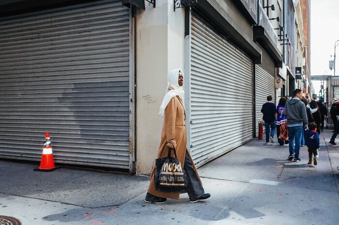 Woman in a beige coat and white headscarf walking on a NYC street, capturing the essence of street photos in the city.