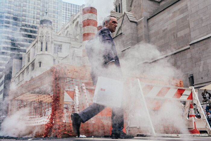 Man walking past construction site with steam rising on a busy NYC street in striking street photos by Mathias Wasik