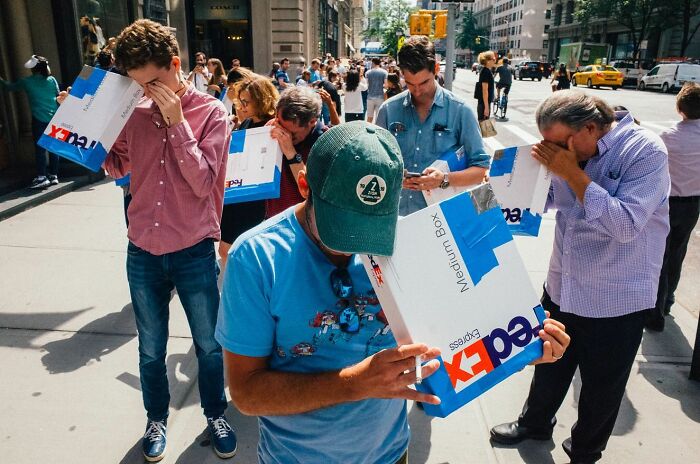 Crowd on busy New York City sidewalk using FedEx boxes to shield their eyes in a striking NYC street photo.