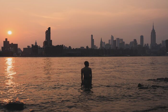 Person standing in water at sunset with NYC skyline in the background, capturing powerful street moments in NYC.