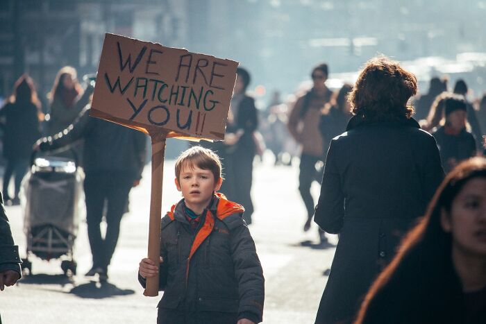 Young boy holding a protest sign in busy NYC street, one of the striking street photos capturing city stories.