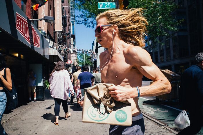 Shirtless man with long hair running on a busy NYC street, captured in a powerful street moment in NYC.