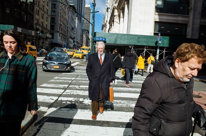 People crossing a busy NYC street with yellow taxis and tall buildings, capturing powerful street moments in NYC.