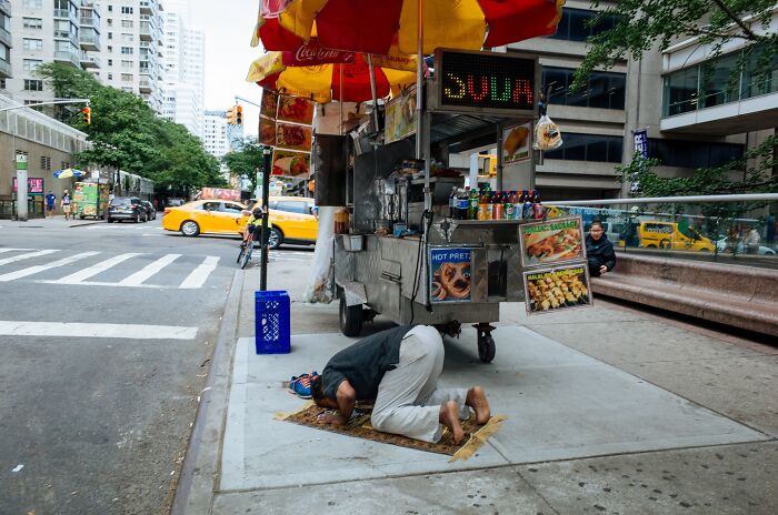 Man praying on the sidewalk near a food cart capturing a powerful street moment in NYC with taxis and pedestrians in the background