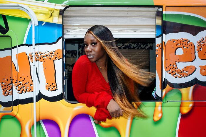 Young woman with long hair leaning out of colorful NYC street art bus window, capturing powerful street moments in NYC.