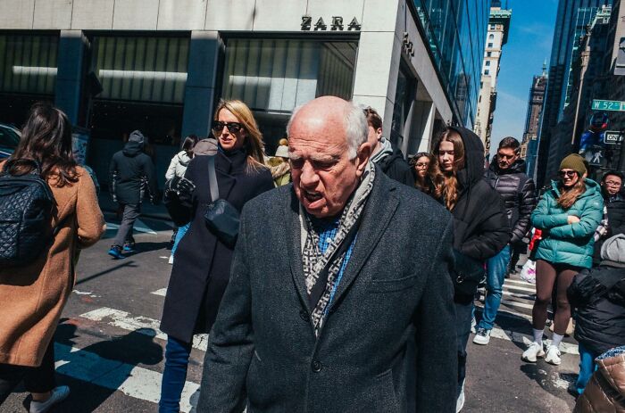 Elderly man walking through busy NYC street with diverse pedestrians, capturing powerful street moments in urban setting.