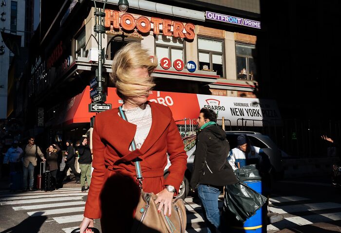 Woman with hair blowing in wind at busy NYC intersection in vibrant street scene capturing powerful NYC moments by photographer.