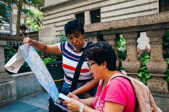 Two women consulting a map and notebook on a busy NYC street, capturing powerful street moments in the city.