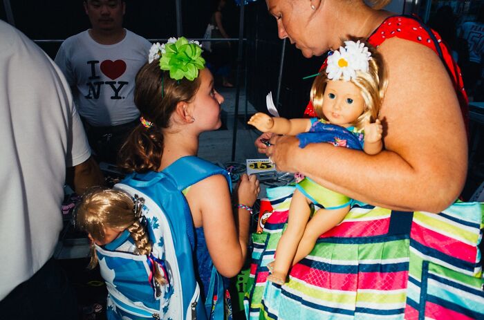 Young girl with doll on backpack and woman holding a doll, street moment captured in NYC by photographer