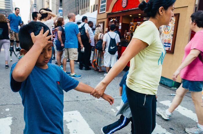 Boy in a blue shirt holding an adult's hand, walking through a crowded NYC street, capturing street photo stories.