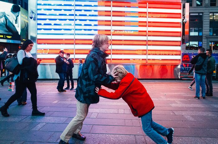 Children play in front of a large illuminated American flag, capturing a striking street photo in NYC’s vibrant cityscape.