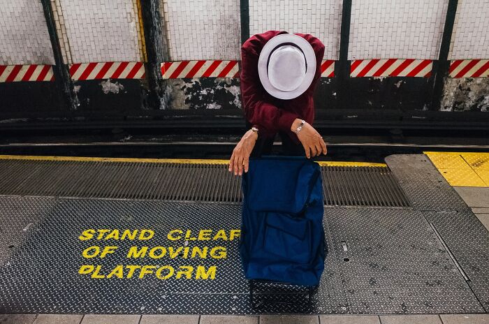 Person in white hat leaning on suitcase at NYC subway platform, one of the striking street photos capturing city stories.