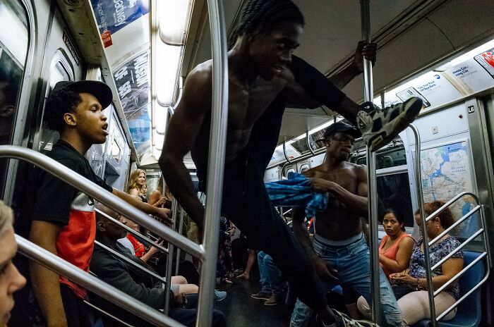 Street photographer captures powerful street moments in NYC subway showing dancers and diverse passengers in motion.