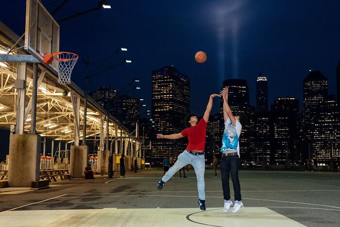 Two young men playing basketball on an outdoor court at night, a powerful street moment in NYC captured.