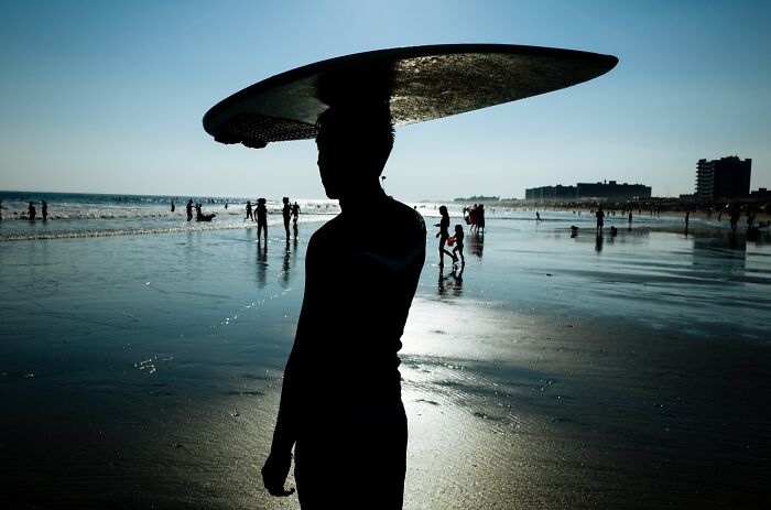 Silhouette of a surfer carrying a board at sunset, one of the powerful street moments of NYC captured by a photographer.